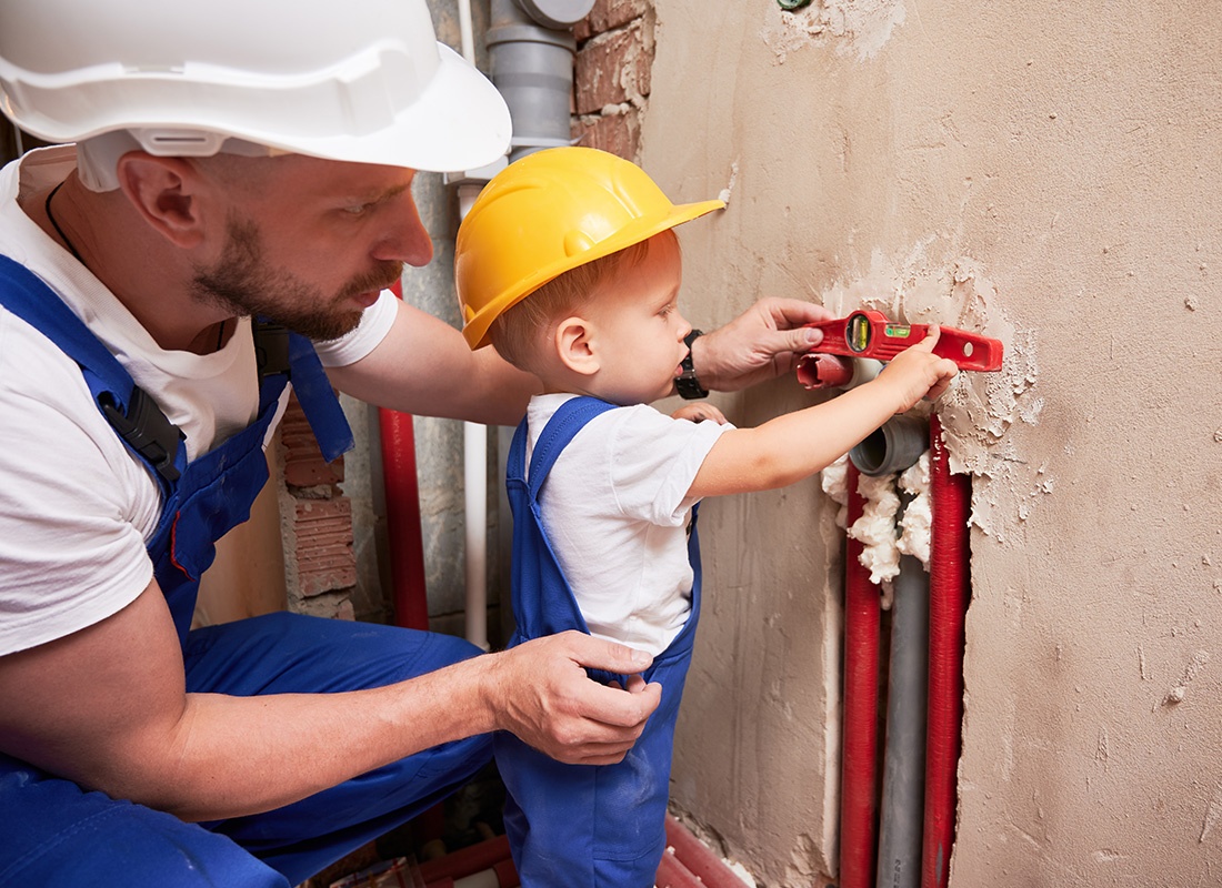 Insurance by Industry - Construction Worker and Baby Using a Level to Measure Pipes in a Wall